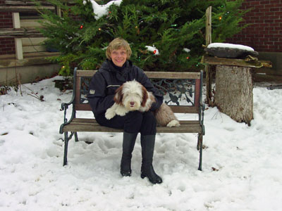 Briana being held by her mommy on a bench placed in front of the evergreens on a snowy day
